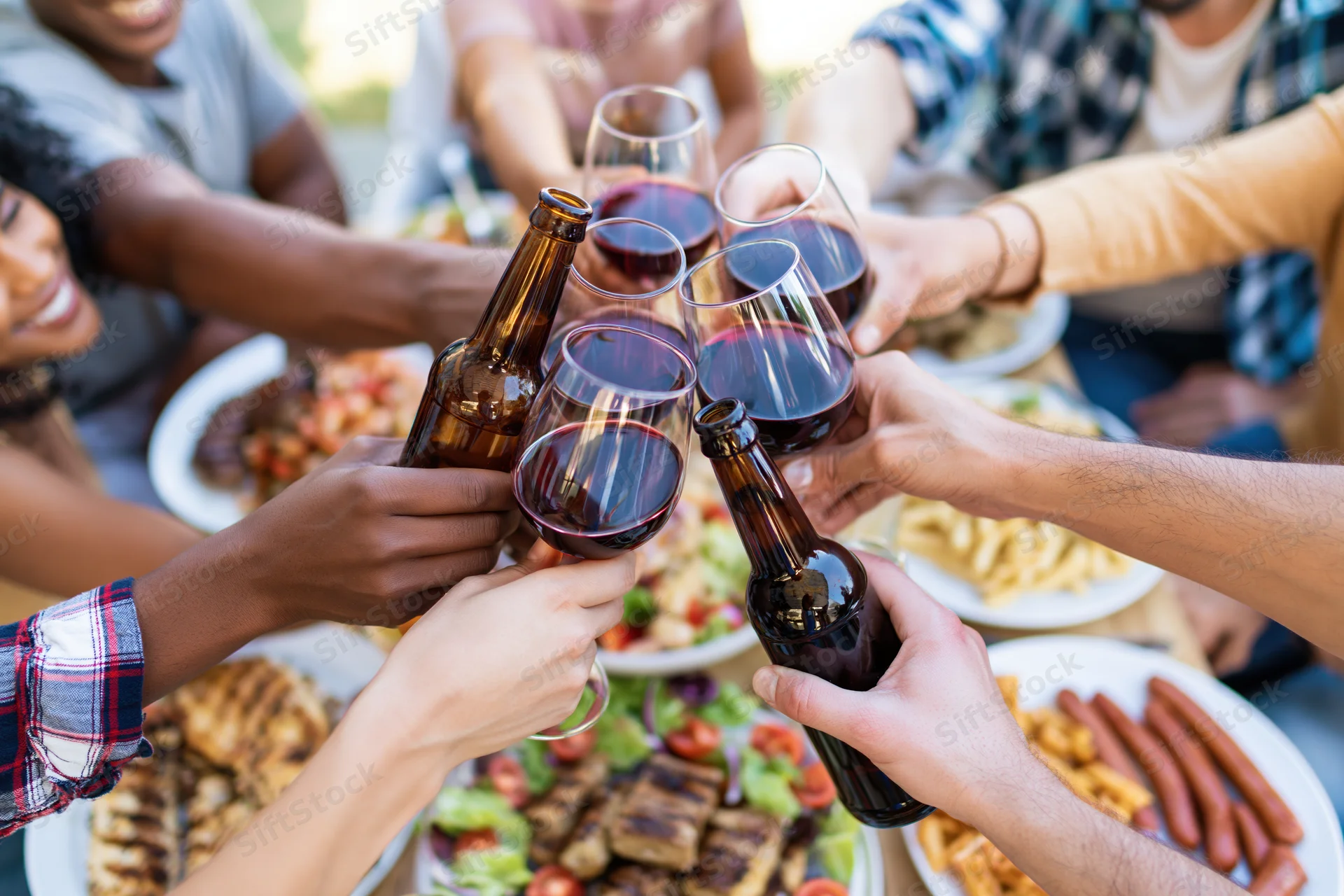 Diverse group toasting with wine and beer over a barbecue meal outdoors