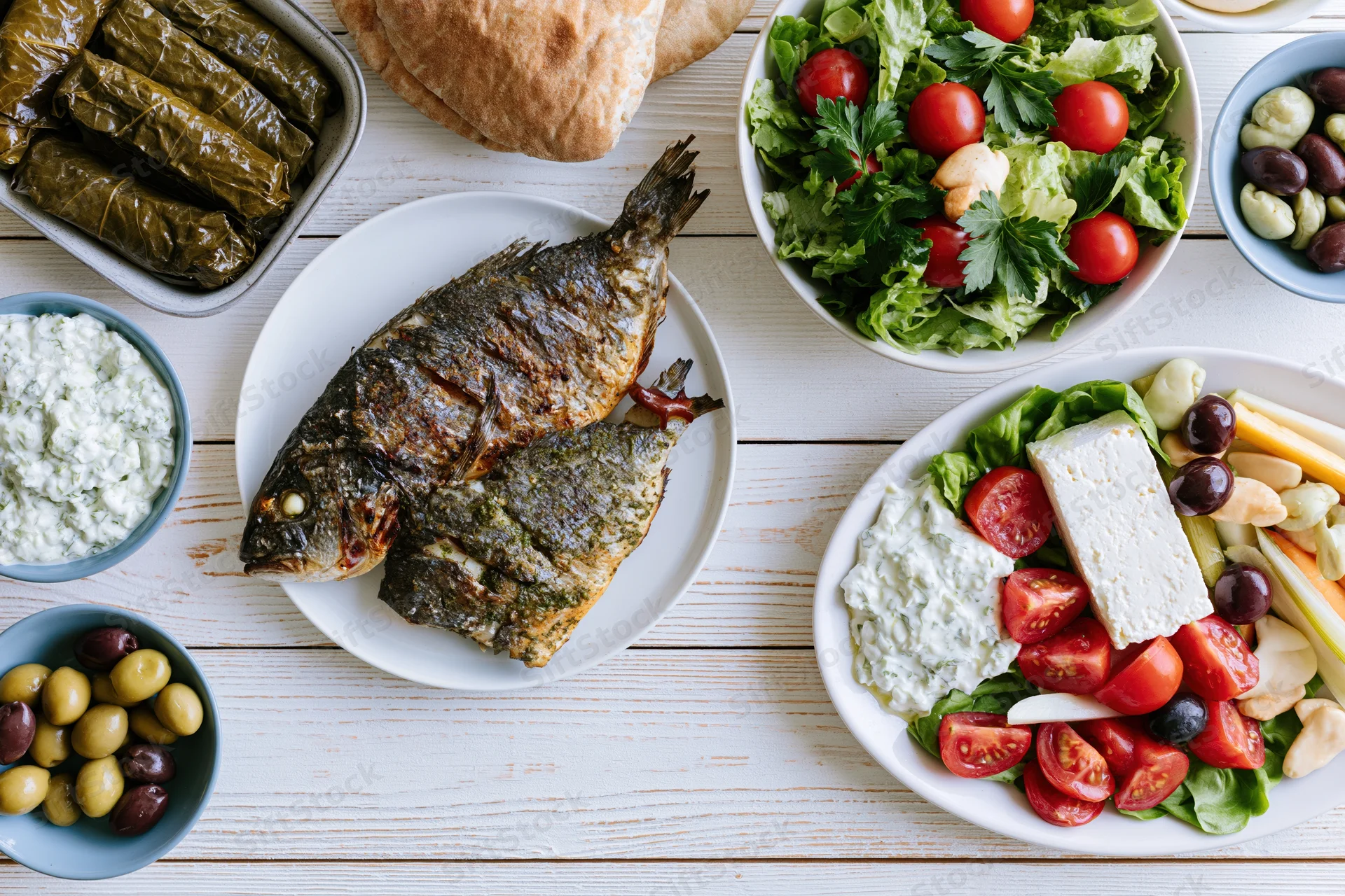 Grilled fish and greek mezze spread arranged on a white wooden table