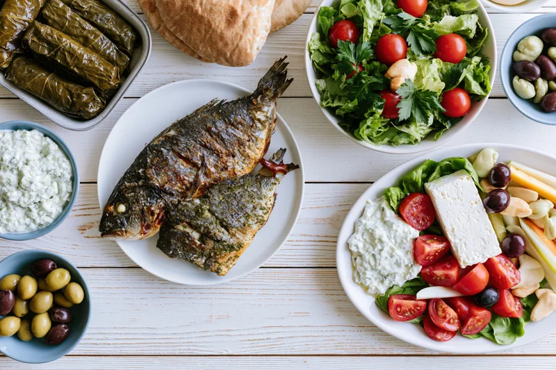 Grilled fish and greek mezze spread arranged on a white wooden table