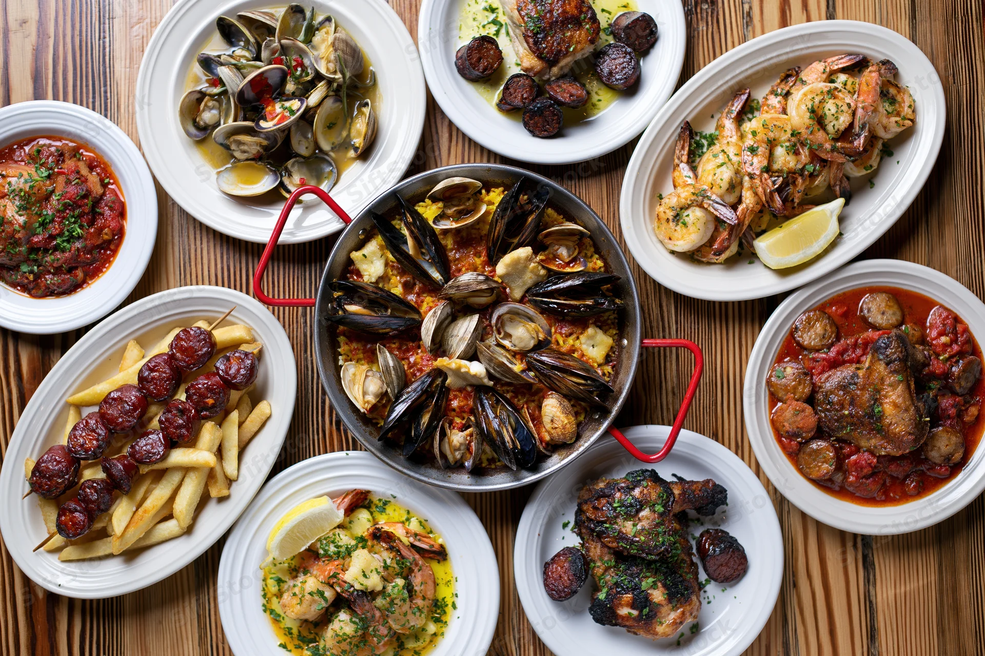 Portuguese seafood spread with paella, clams, shrimp, chicken, and fries arranged on a wooden table in overhead flat-lay view