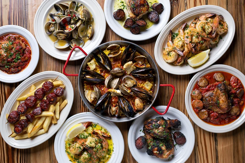 Portuguese seafood spread with paella, clams, shrimp, chicken, and fries arranged on a wooden table in overhead flat-lay view