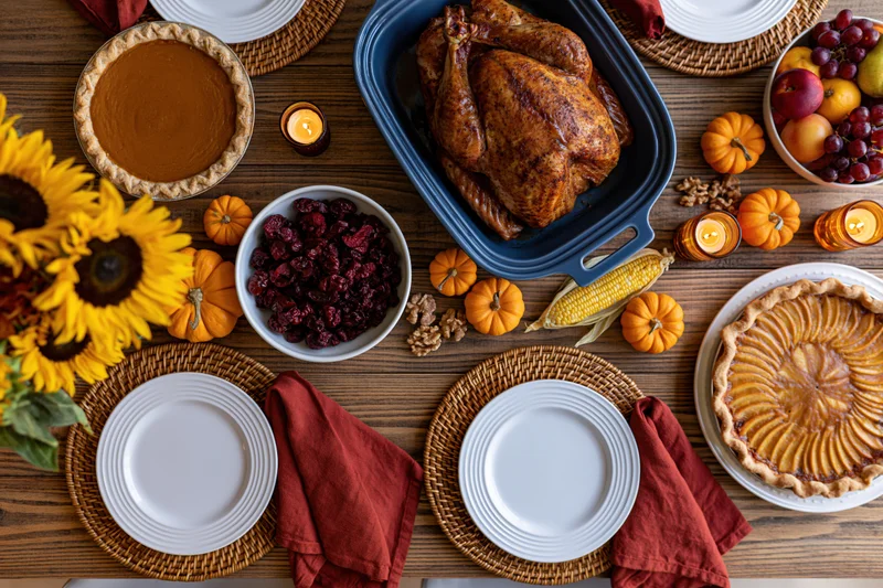 Overhead view of a thanksgiving dinner table set with roasted turkey, pumpkin pie, cranberries, corn, and autumn decorations on a wooden surface