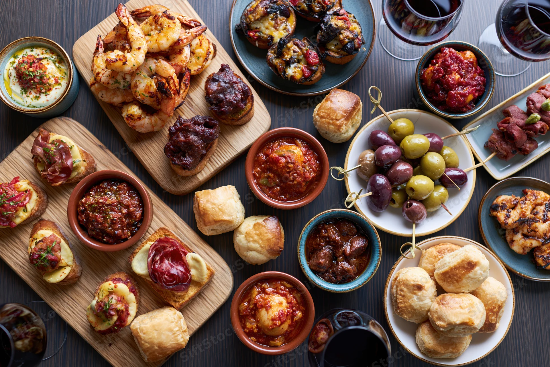 Overhead view of a spanish tapas spread with shrimp, olives, crostini, and wine on a dark wooden table