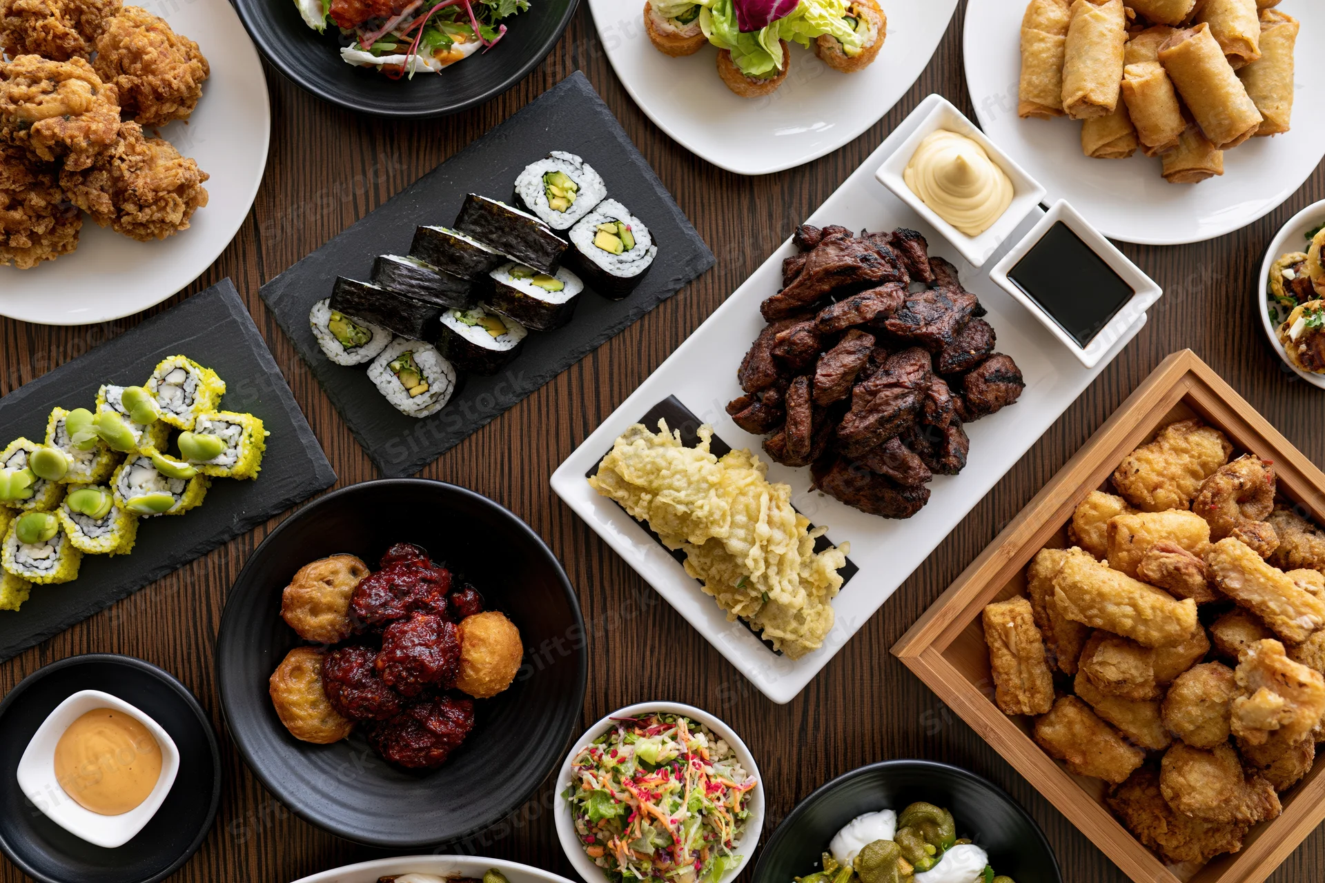 Overhead view of a restaurant table filled with various dishes including sushi, fried items, and appetizers arranged on plates and trays