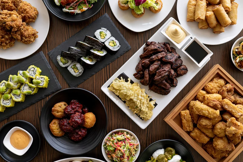 Overhead view of a restaurant table filled with various dishes including sushi, fried items, and appetizers arranged on plates and trays