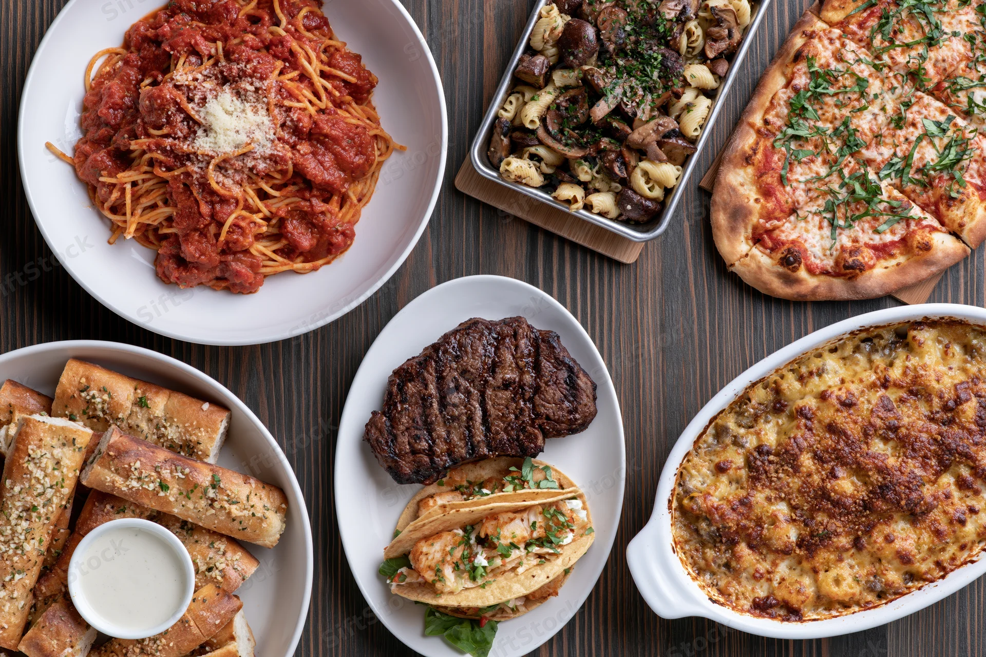 Overhead flat-lay of various Italian-American dishes arranged on a dark wooden table