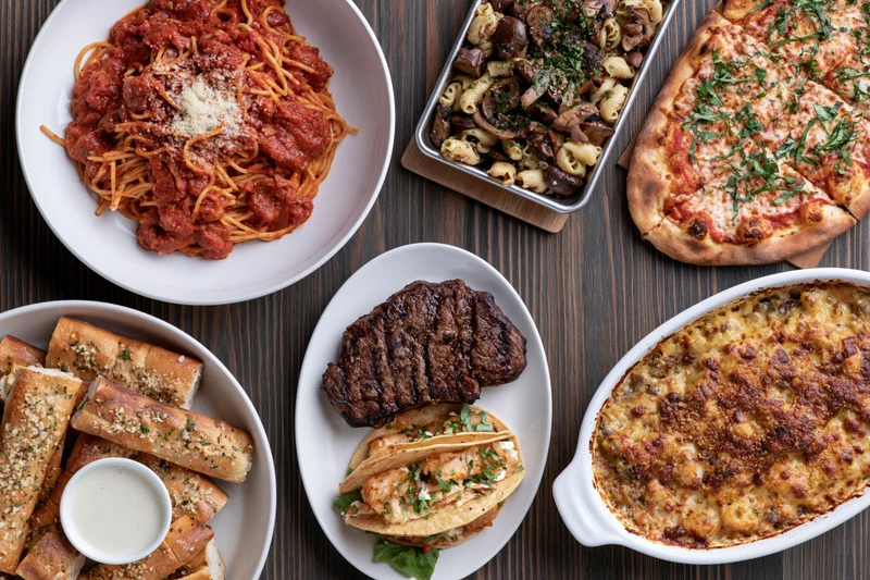 Overhead flat-lay of various Italian-American dishes arranged on a dark wooden table