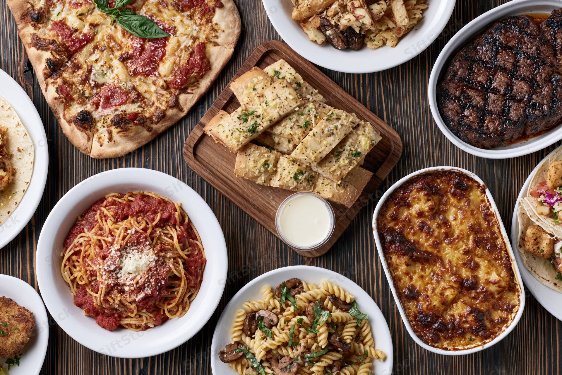 Overhead flat-lay of various Italian-American dishes arranged on a dark wooden table