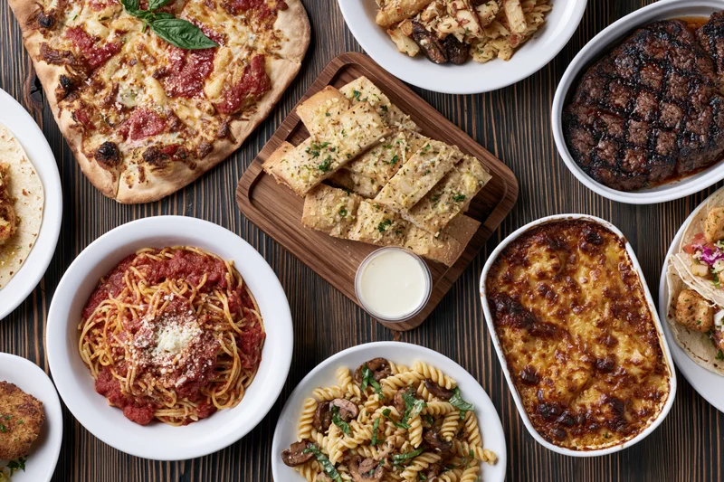 Overhead flat-lay of various Italian-American dishes arranged on a dark wooden table