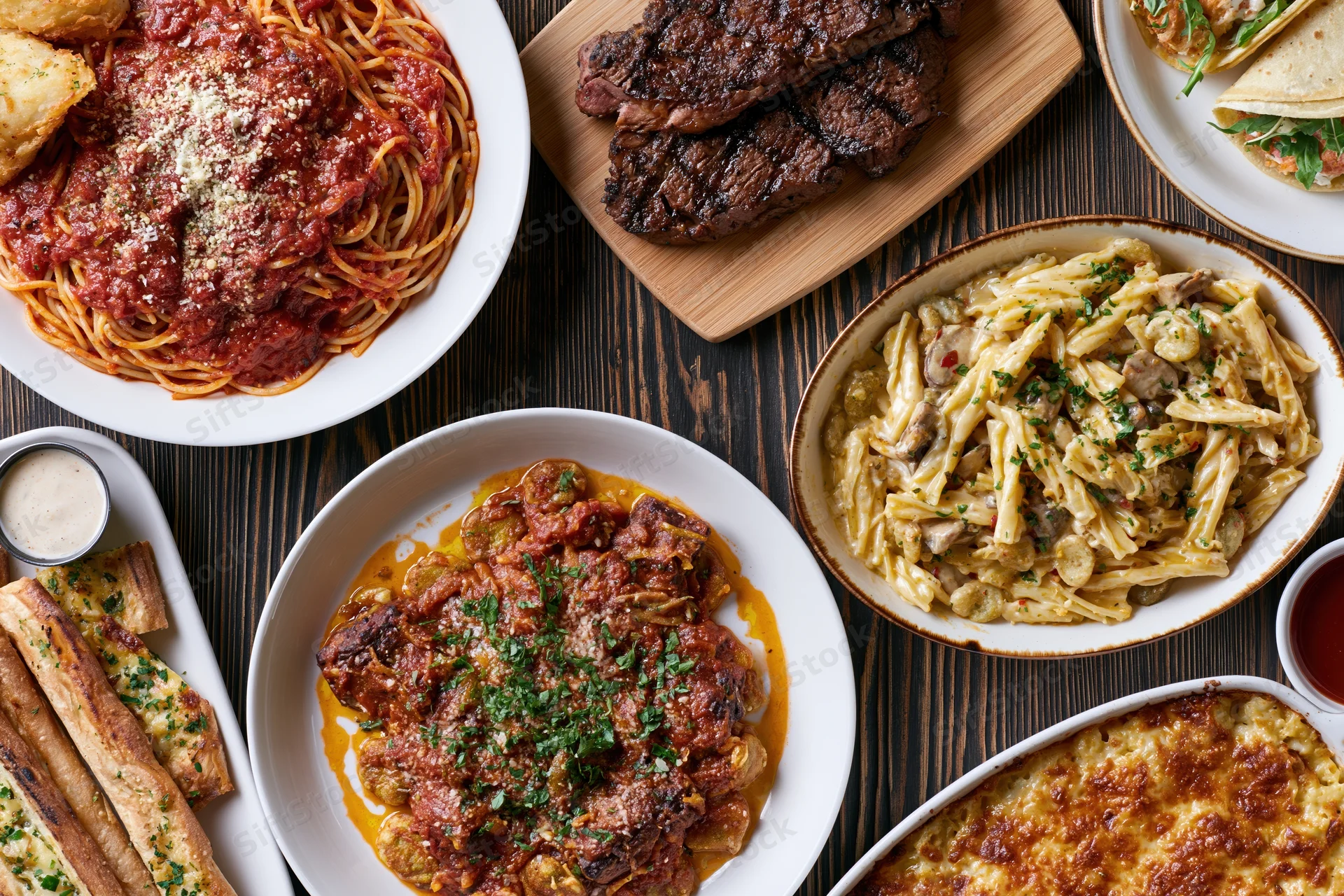 Overhead flat-lay of multiple Italian-American dishes served on a dark wooden table