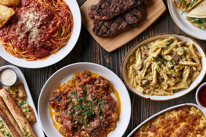 Overhead flat-lay of multiple Italian-American dishes served on a dark wooden table