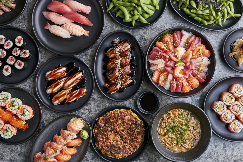 Overhead flat-lay of a large Japanese omakase spread covering a table with various sushi, sashimi, and side dishes on black plates