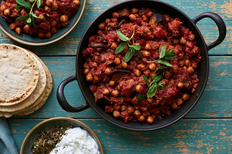 Chickpea stew in a black cast-iron skillet with mint garnish on a blue wooden table, served with flatbread and yogurt side dishes