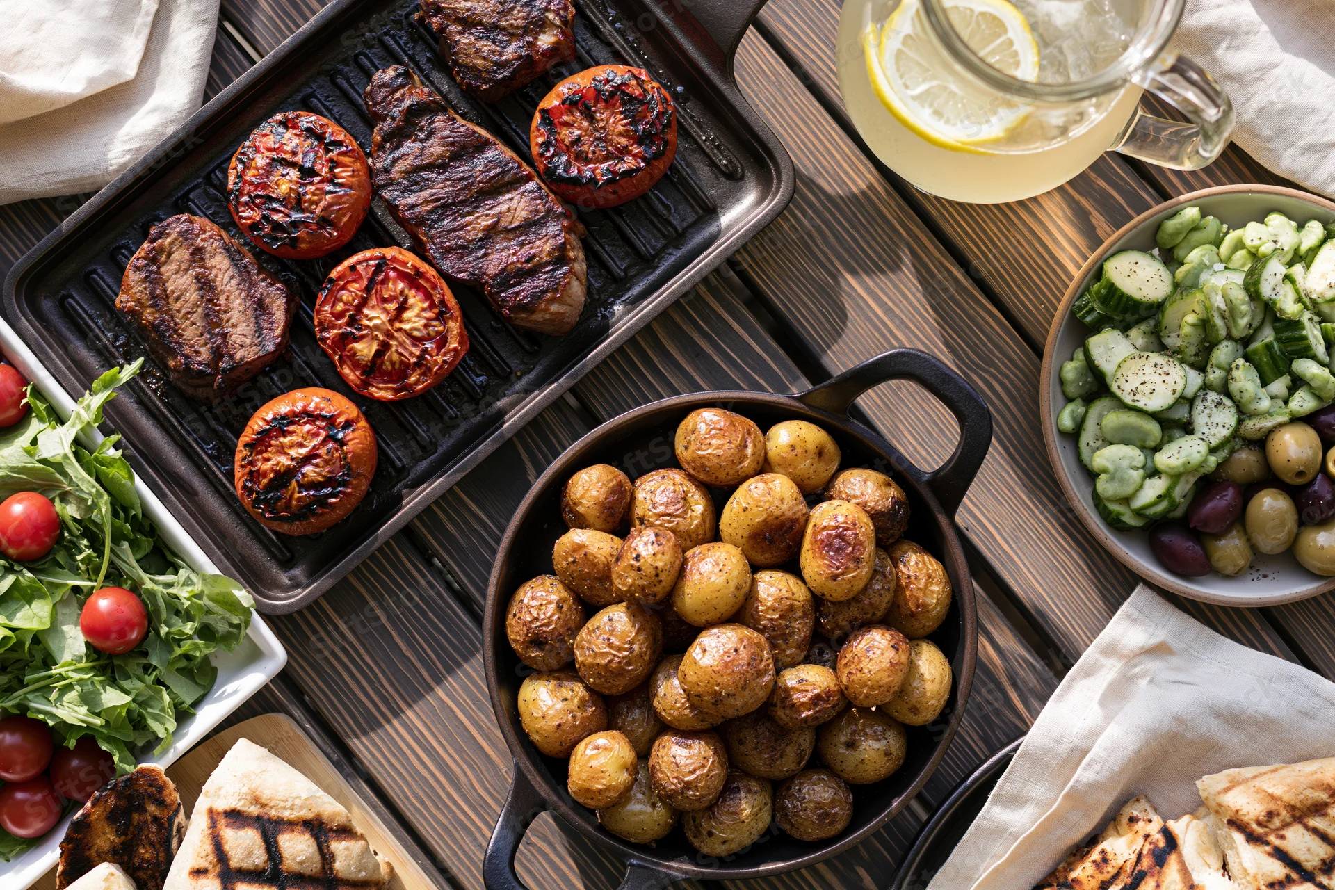 Grilled steak and vegetables served on a dark wooden table with side dishes and lemon drink