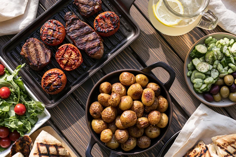 Grilled steak and vegetables served on a dark wooden table with side dishes and lemon drink