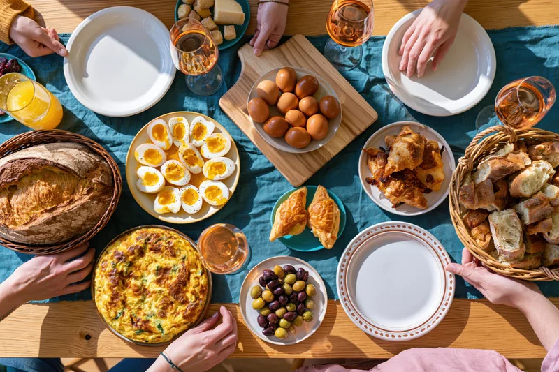 Overhead view of a shared spanish tapas breakfast spread on a wooden table with hands reaching for plates and food