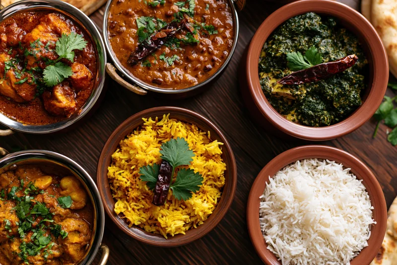 Overhead flat-lay of an indian feast with curries, rice, and naan on a dark wooden table