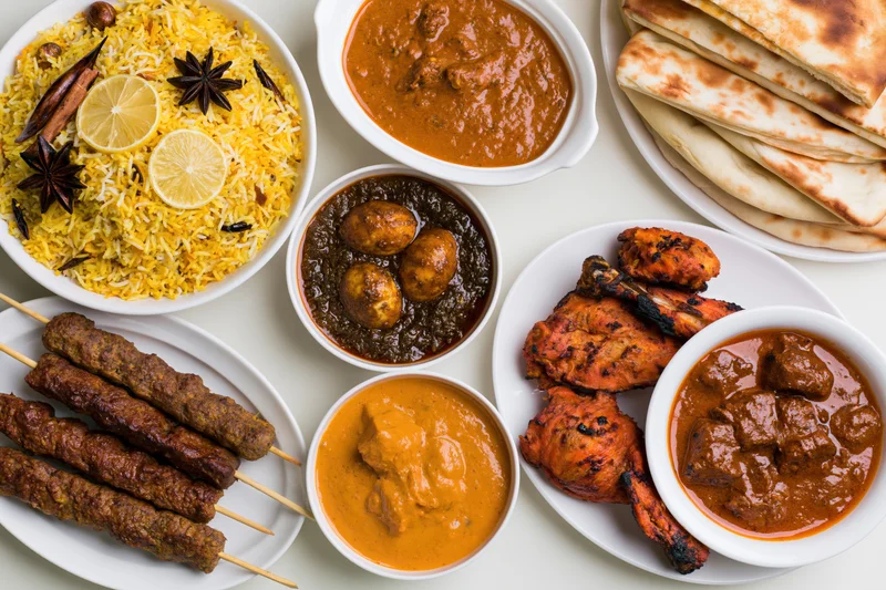 Overhead flat-lay of an indian nonvegetarian feast spread with biryani, curries, kebabs, tandoori chicken, and naan on white plates
