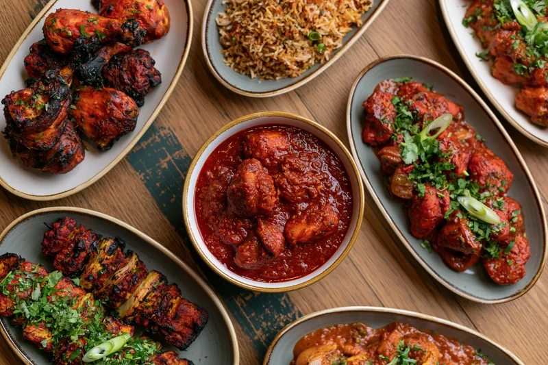 Overhead view of an indian restaurant spread with tandoori chicken, curry, biryani and garnished dishes on a wooden table