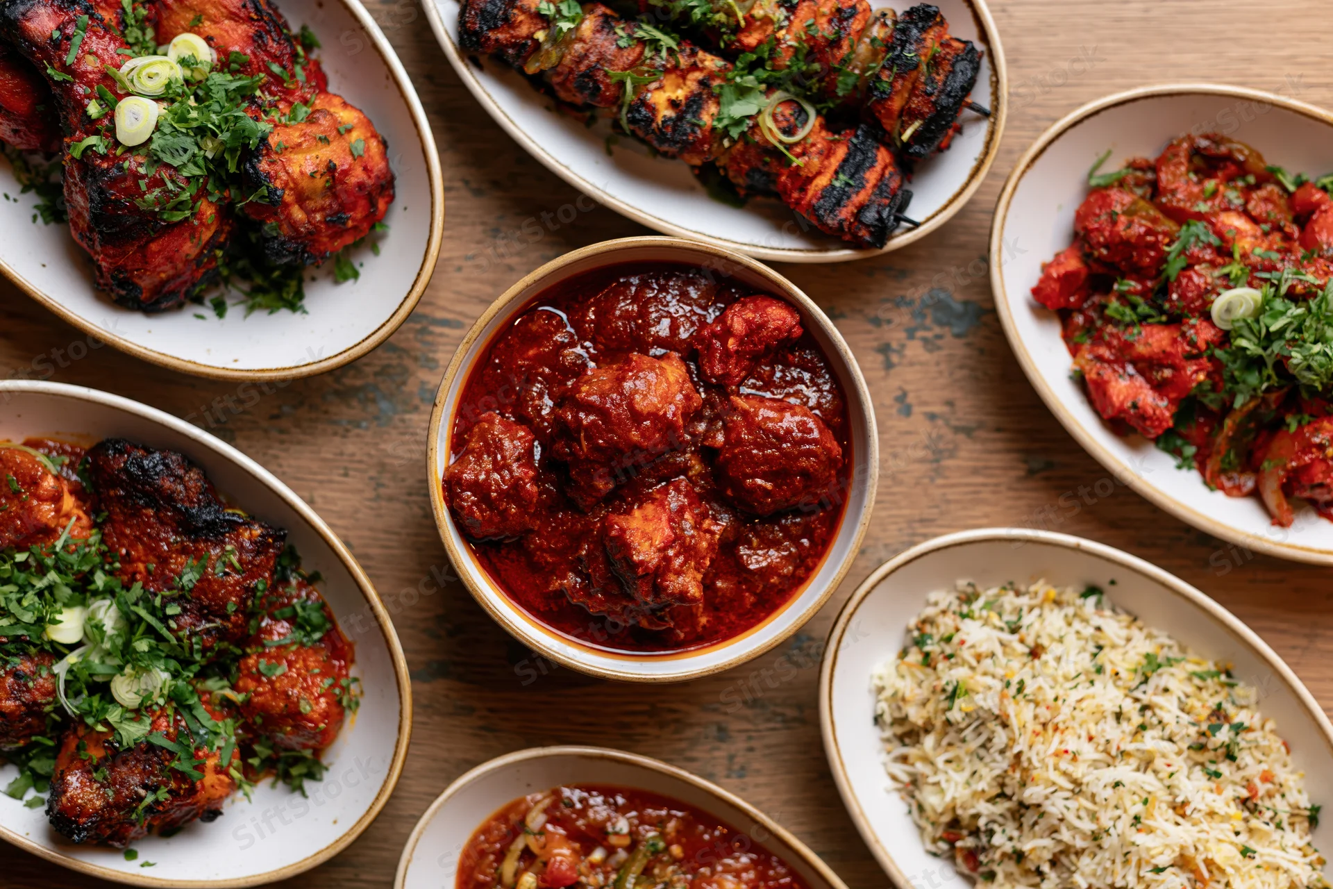 Overhead flat-lay of indian restaurant dishes arranged on wooden table