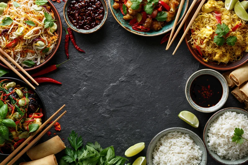 Assorted asian dishes arranged in a border around a dark slate surface with copyspace in center