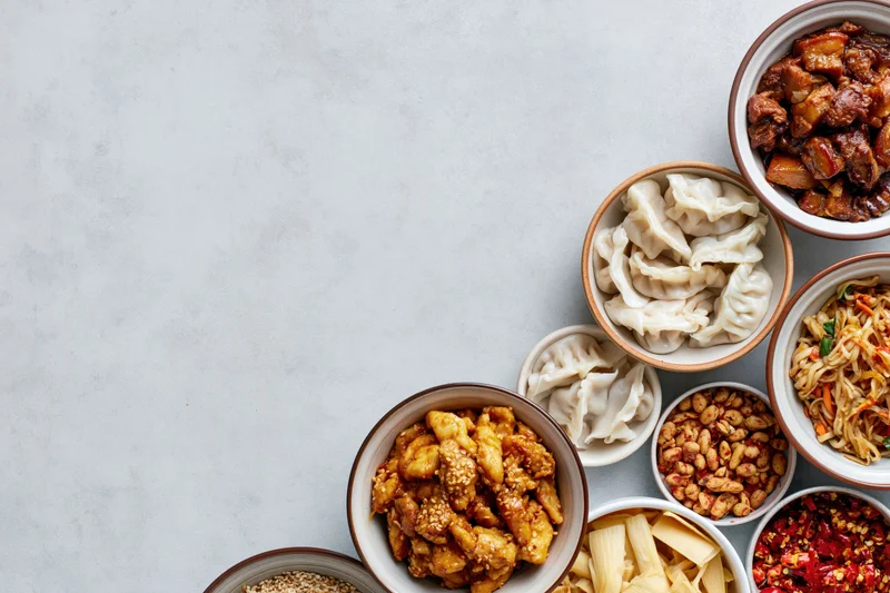 Assorted chinese dishes in bowls arranged along the right side of a light gray surface