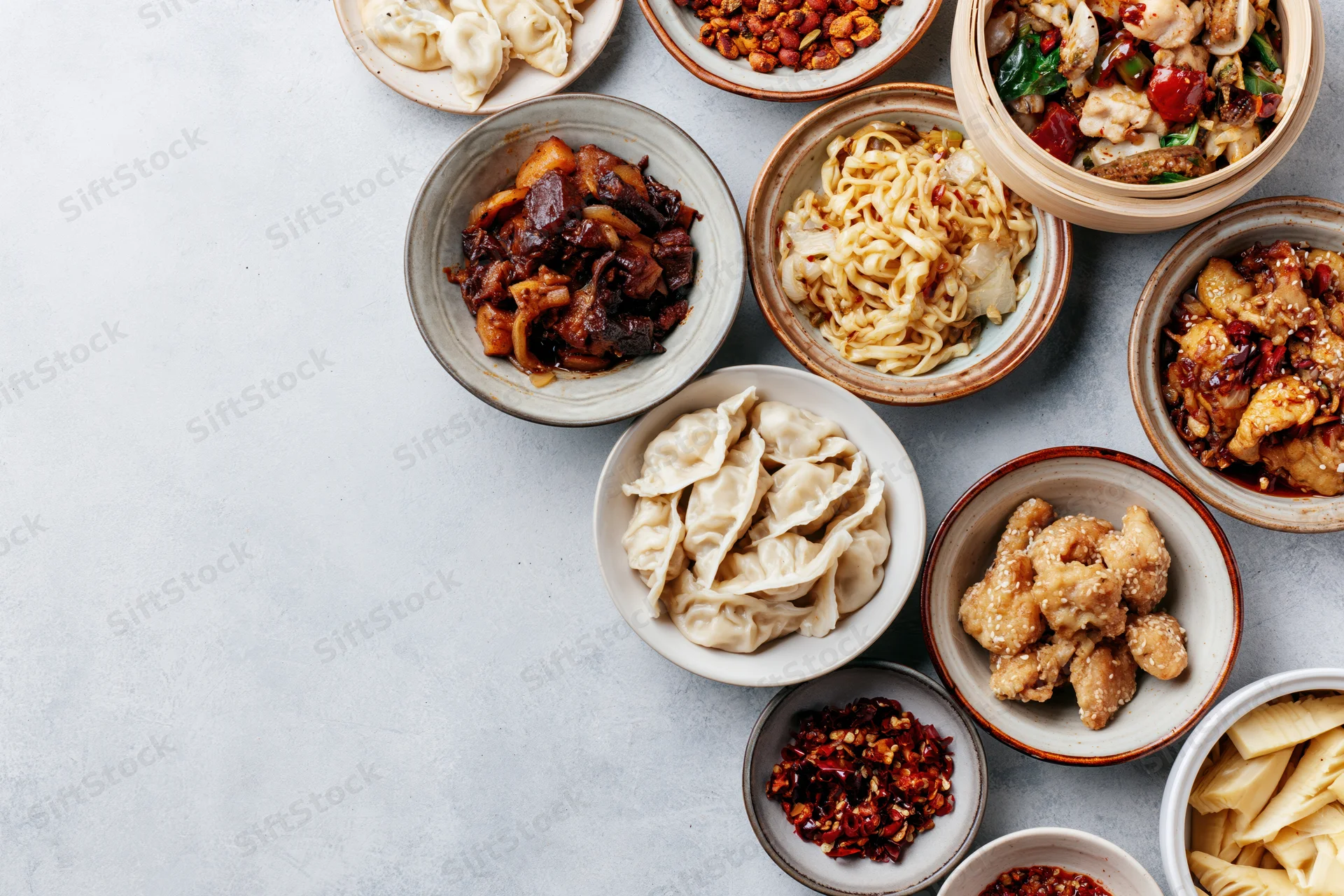 Assorted chinese dishes arranged in ceramic bowls on a gray surface in overhead flat lay view
