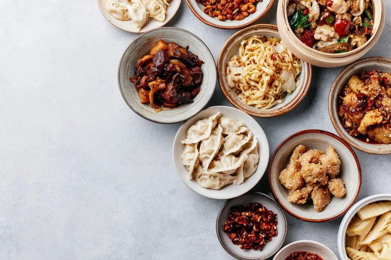 Assorted chinese dishes arranged in ceramic bowls on a gray surface in overhead flat lay view