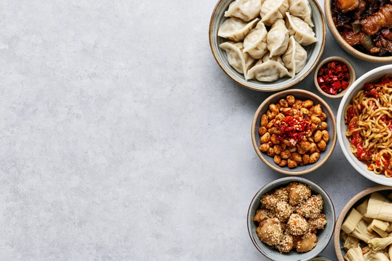 Assorted chinese dishes arranged in bowls on a gray surface in overhead flat-lay view