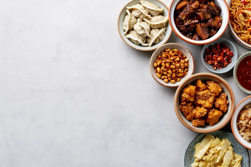 Assorted chinese dishes arranged in bowls on a white surface in overhead flat lay view