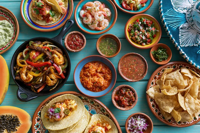 Overhead flat-lay of assorted traditional Mexican dishes on a blue wooden table