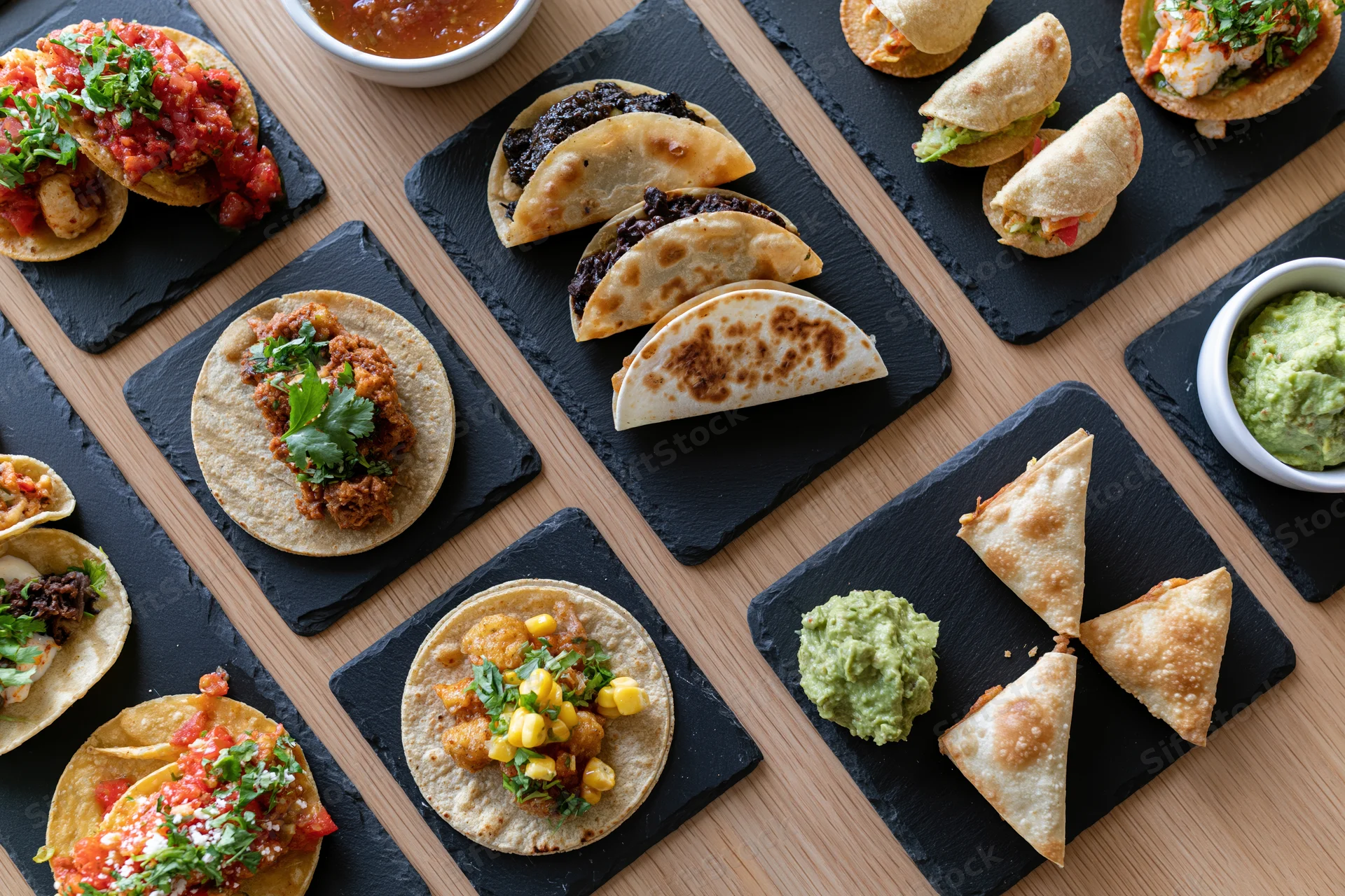 Overhead flat-lay of assorted mexican dishes arranged on slate boards on wooden table
