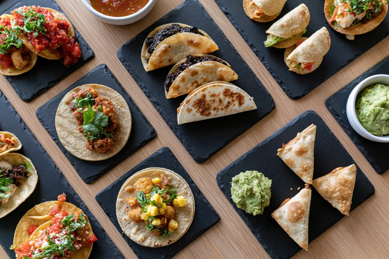 Overhead flat-lay of assorted mexican dishes arranged on slate boards on wooden table
