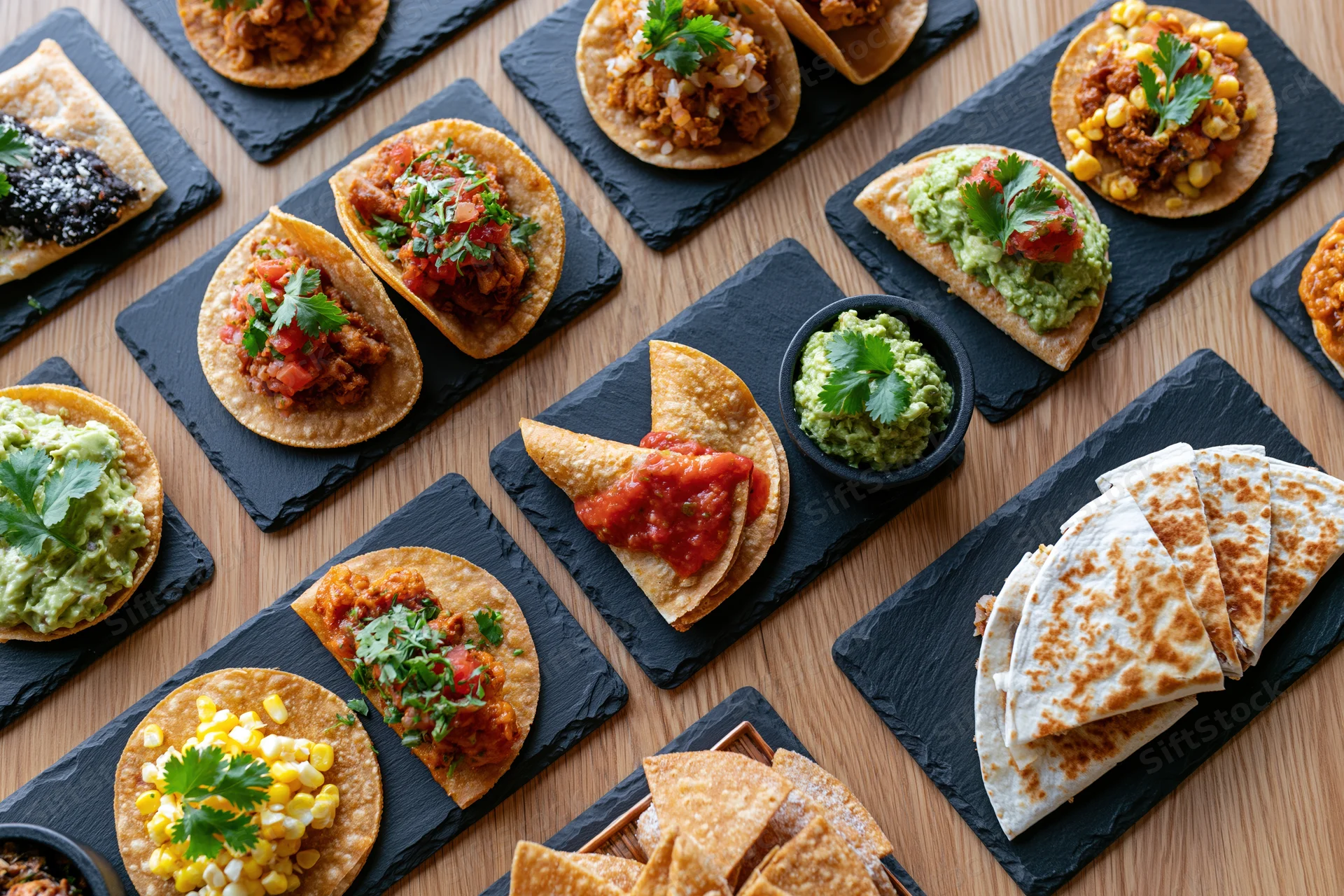 Overhead flat-lay of multiple mexican restaurant dishes arranged on slate boards on wooden table