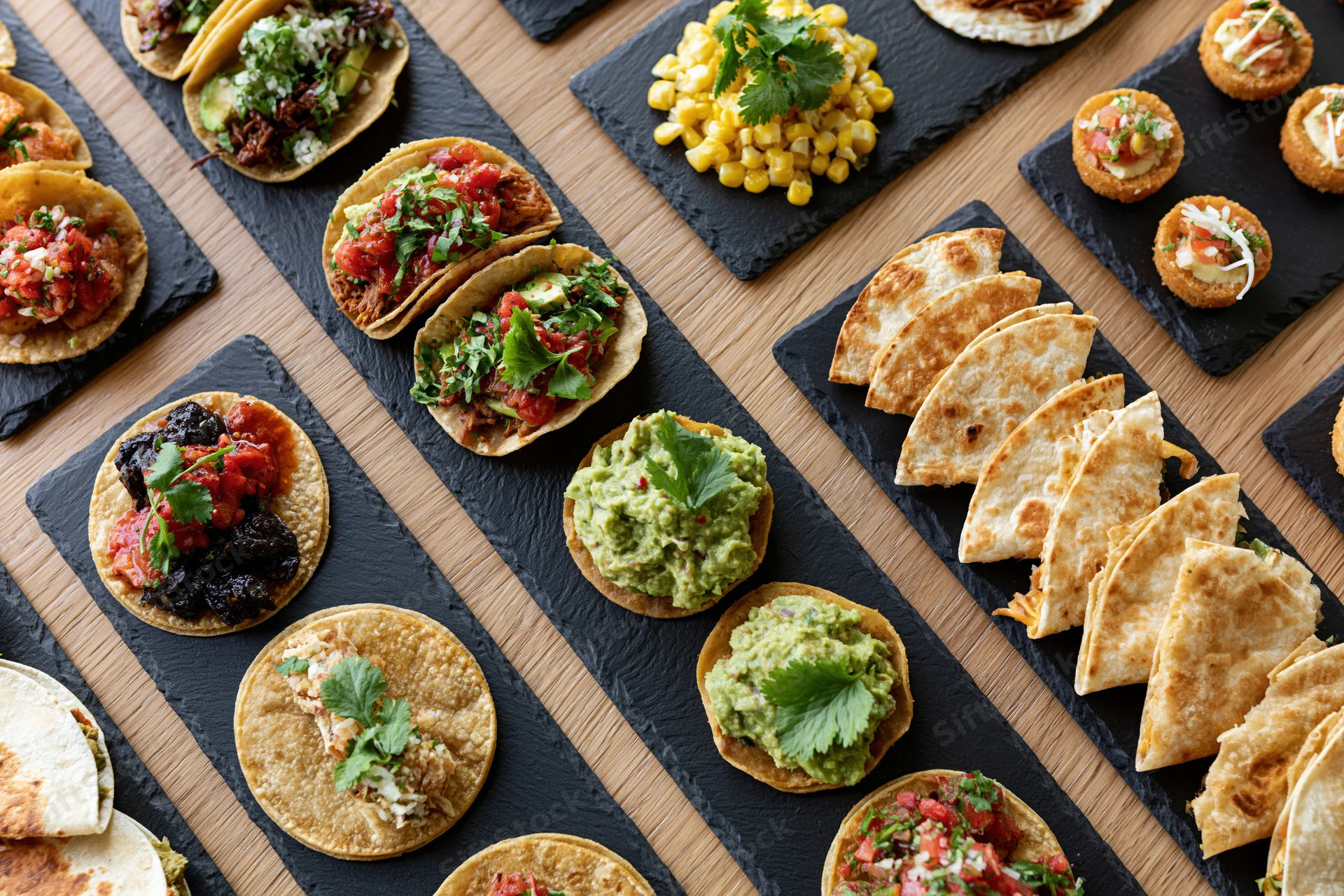 Overhead flat-lay of assorted mexican dishes arranged on slate platters on wooden table