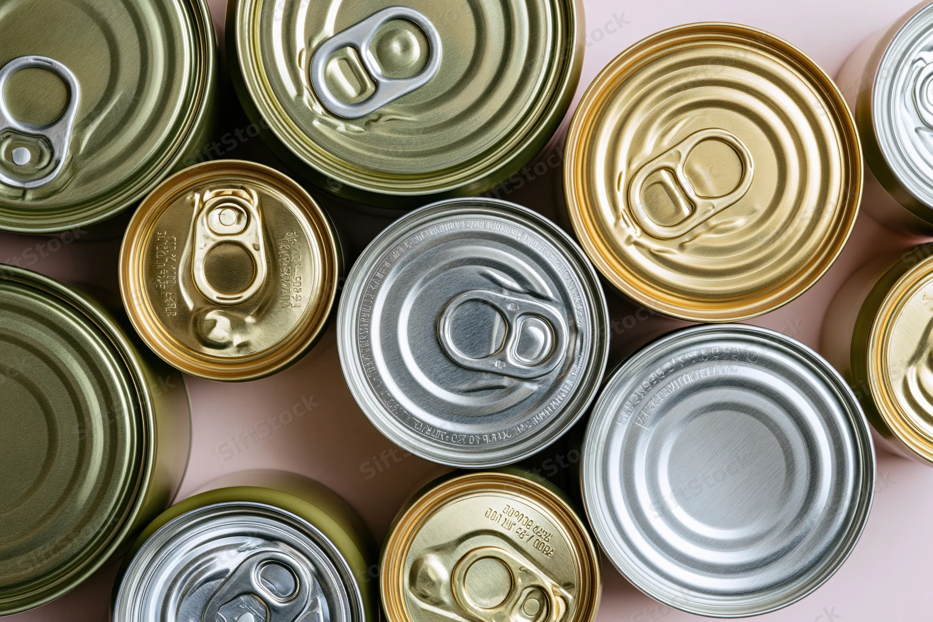 Overhead flat-lay of multiple metal food cans arranged closely on a pink surface