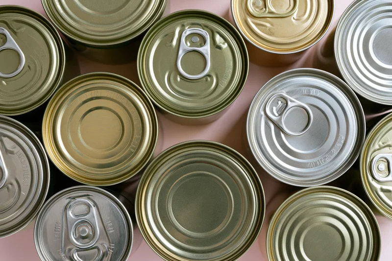 Overhead flat-lay of multiple metal food cans arranged closely on a pink surface