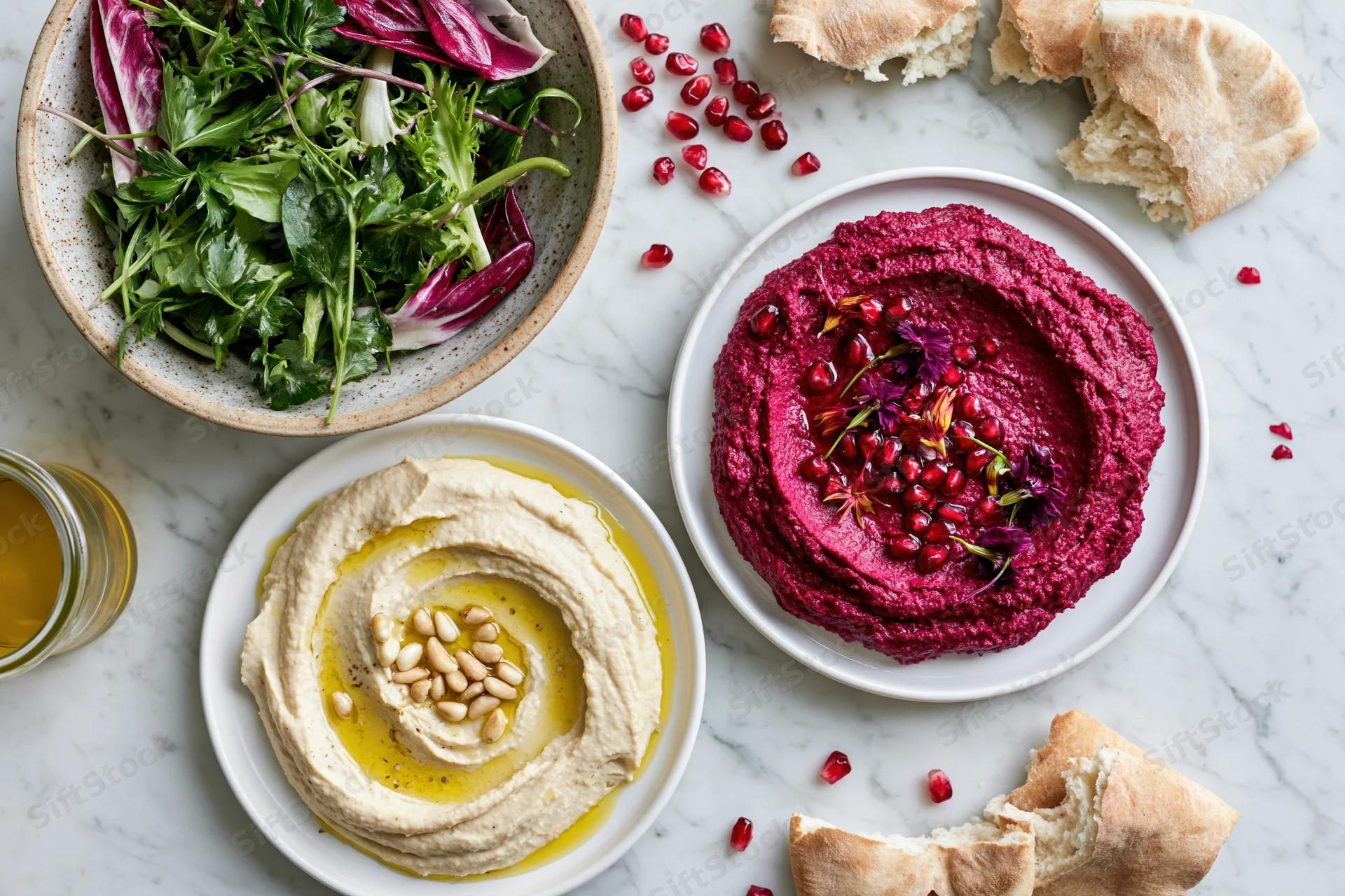 Three mezze plates with hummus, beetroot dip and salad arranged on white marble surface