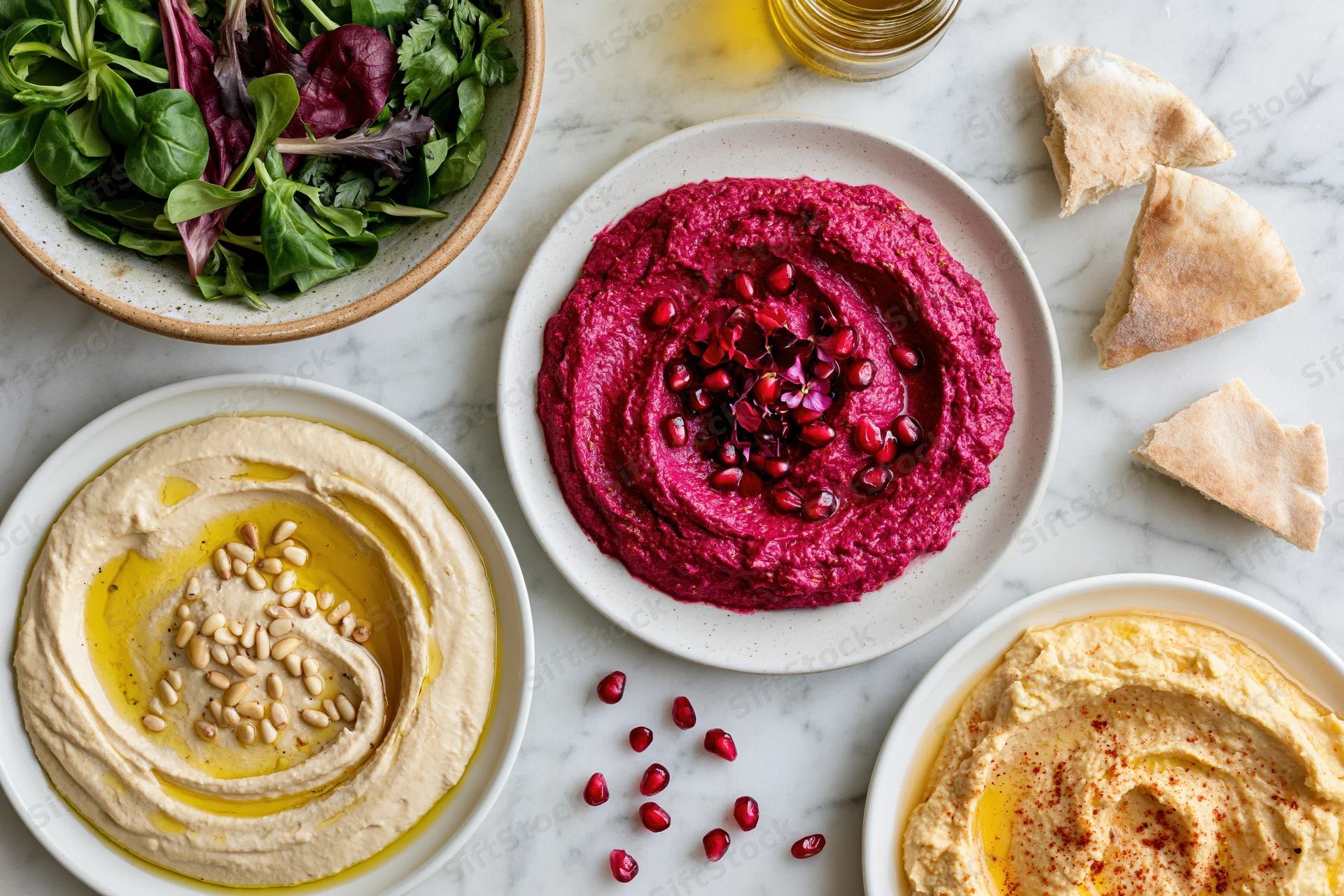 Three mezze plates with hummus, beet dip, and salad arranged on a white marble surface
