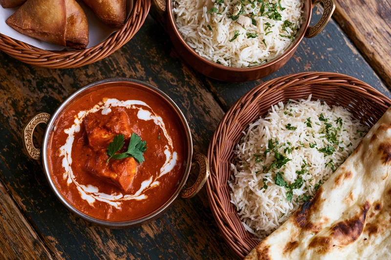 Overhead flat lay of indian restaurant meal with curry, rice, naan and samosas on a worn wooden table