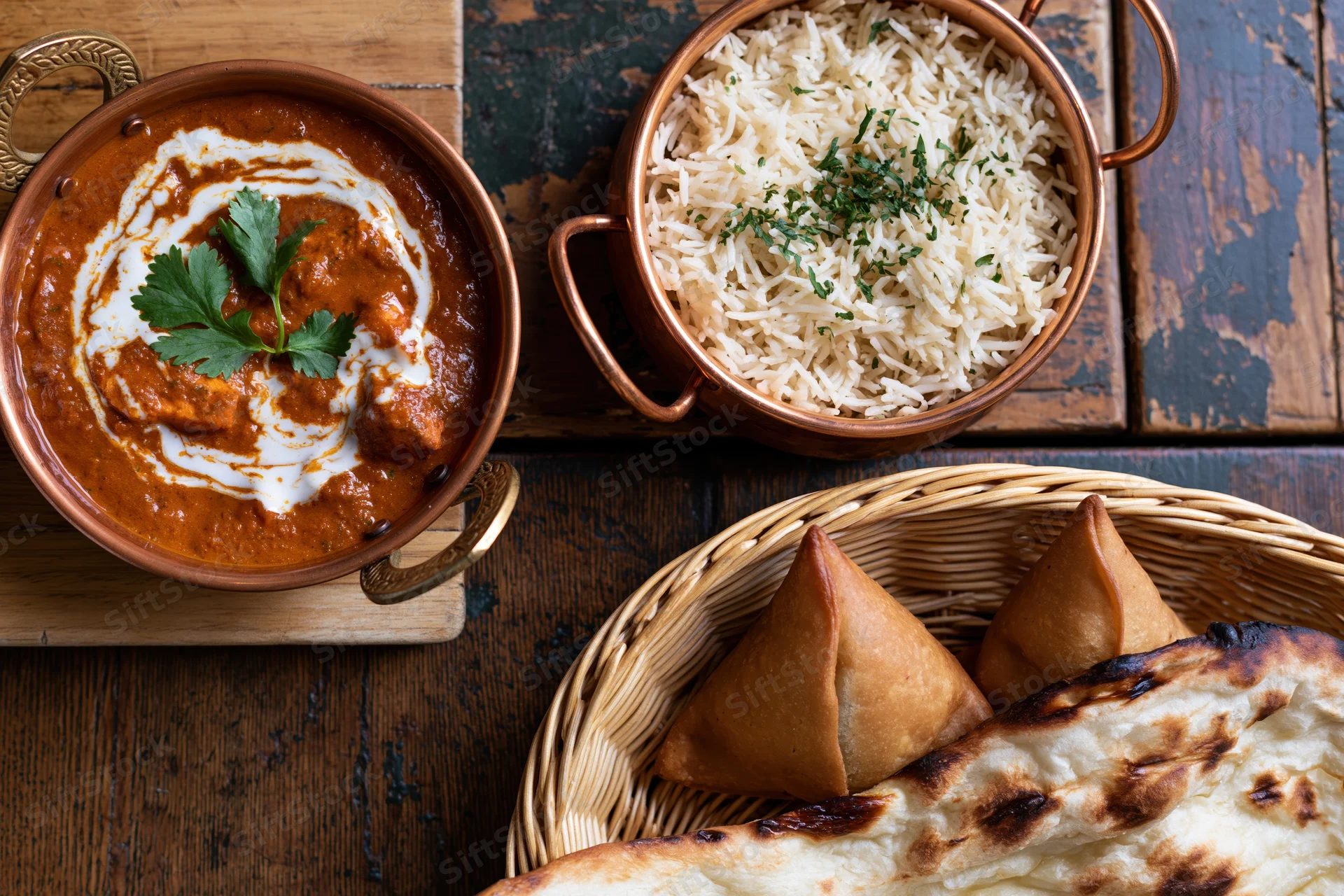 Indian meal with curry, rice, naan and samosas arranged on wooden table in overhead flat lay