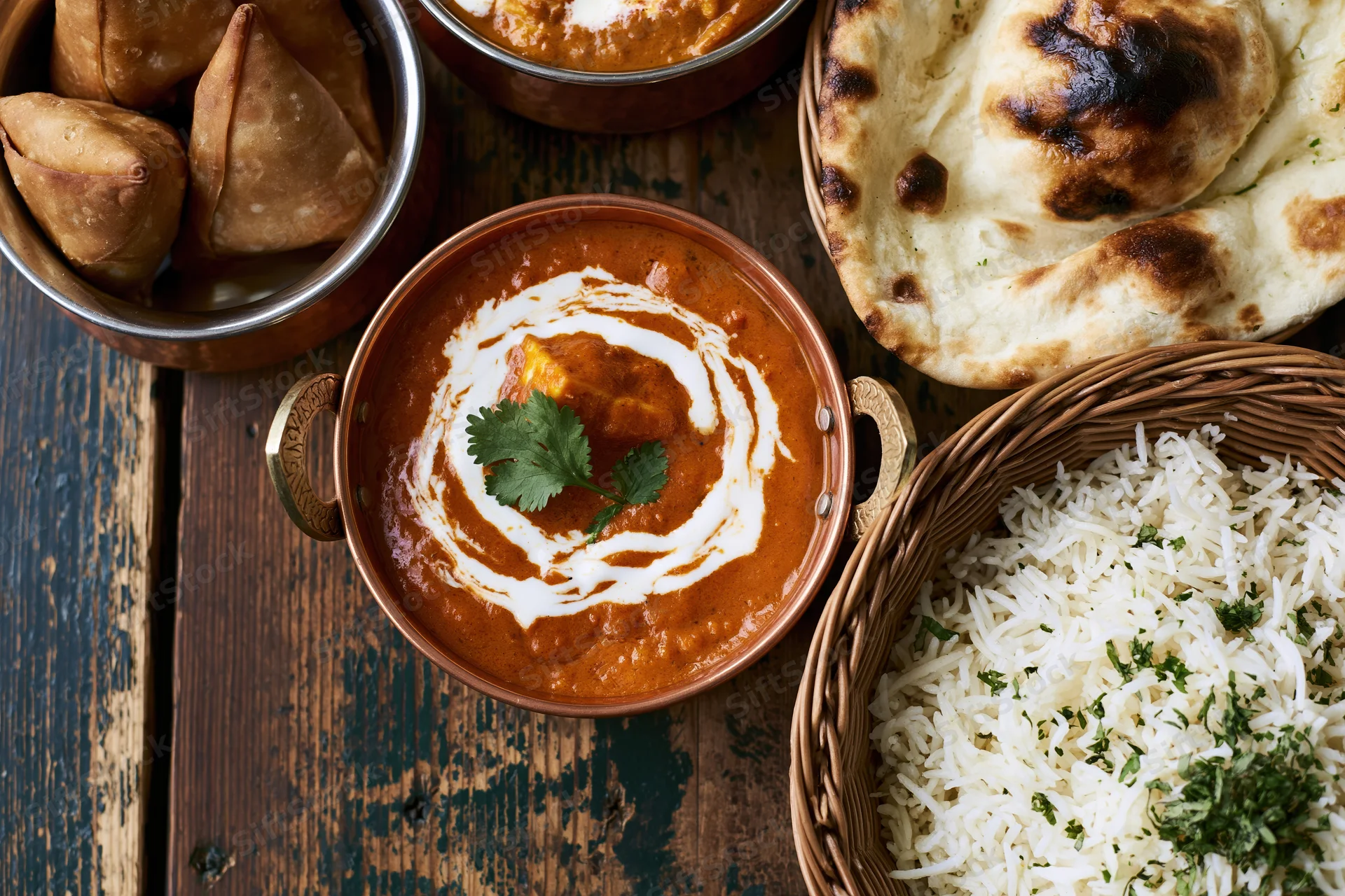 Indian meal spread with curry, rice, naan and samosas on rustic wooden table