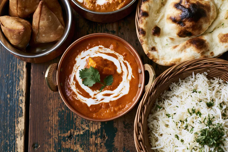 Indian meal spread with curry, rice, naan and samosas on rustic wooden table