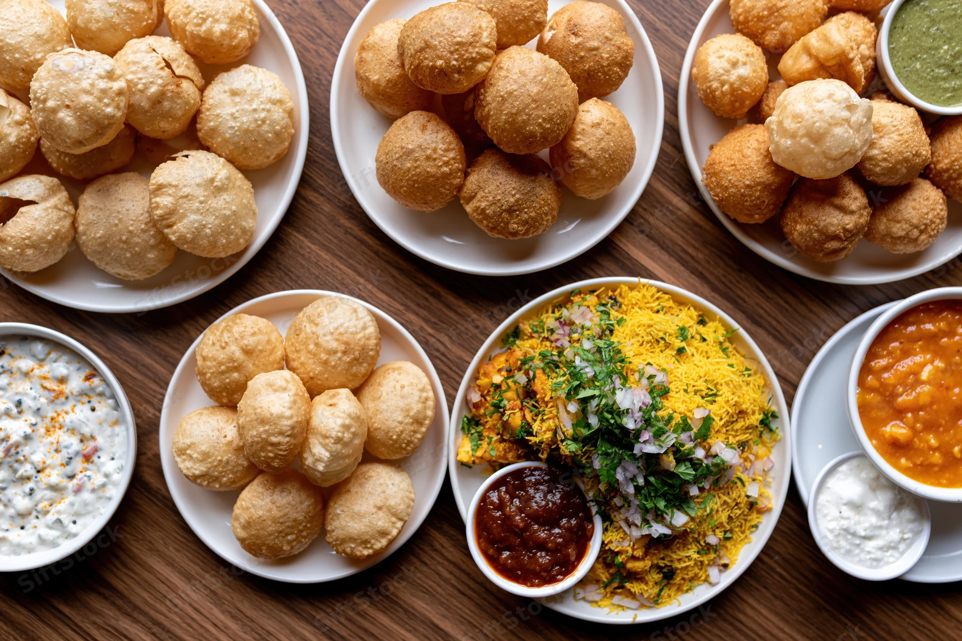 Overhead flat lay of pani puri and dahi with chutneys and garnishes on wooden table