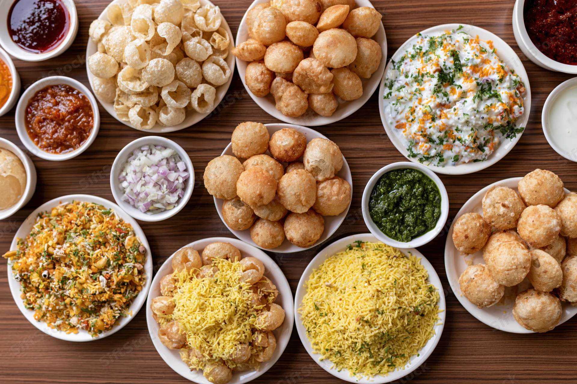 Overhead flat lay of indian street food spread featuring pani puri, dahi, chutneys, and snacks on wooden table
