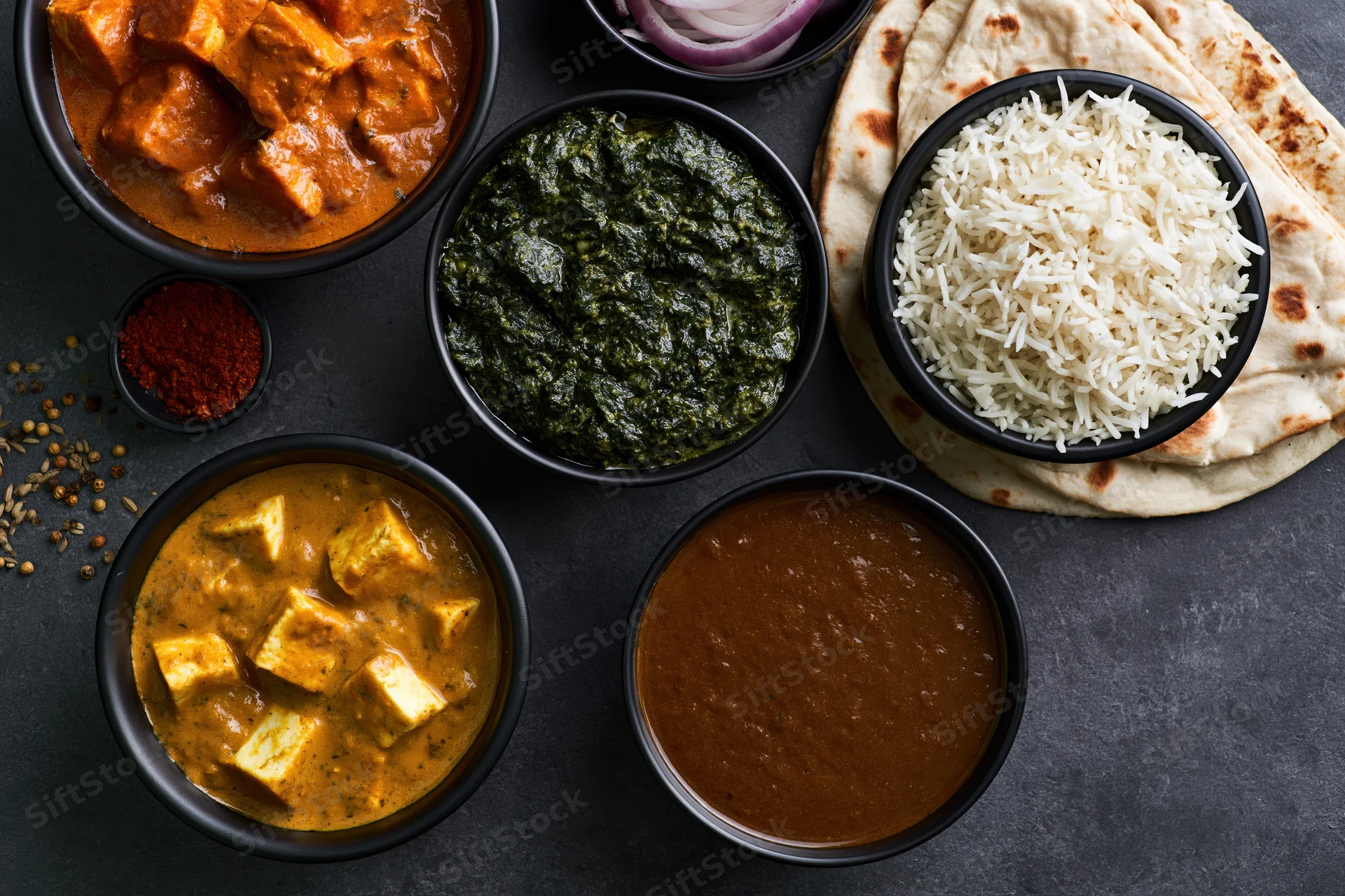 Overhead flat lay of indian vegetarian meal with curry, rice, naan and bowls on dark surface