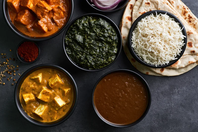 Overhead flat lay of indian vegetarian meal with curry, rice, naan and bowls on dark surface