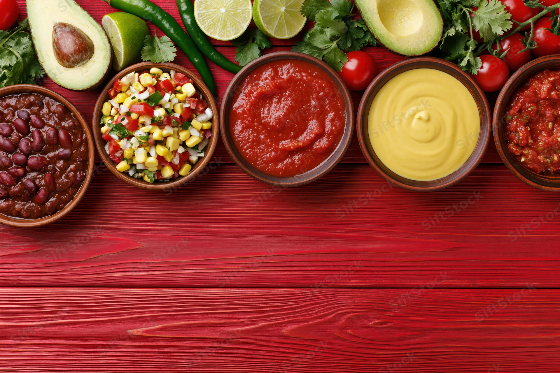 Overhead flat lay of mexican dips and condiments arranged on red wooden table with copyspace below