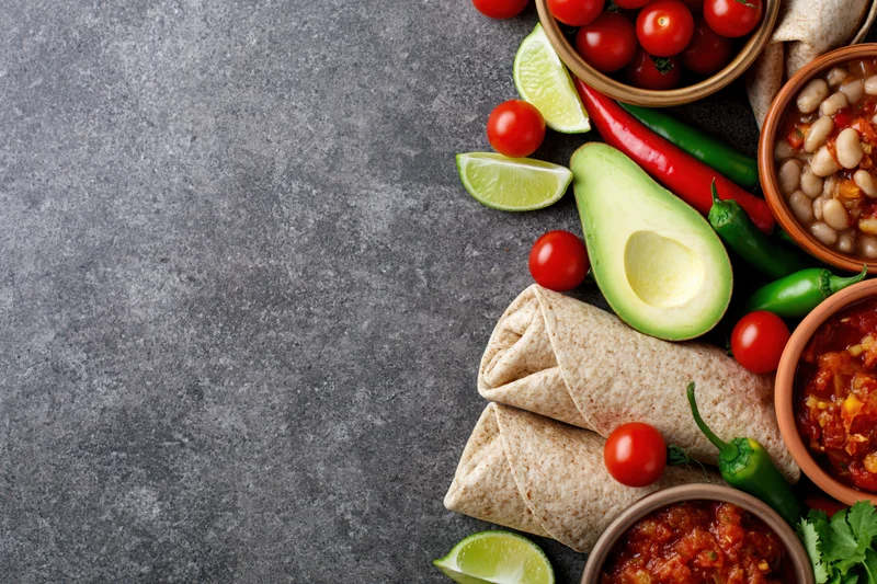 Mexican food ingredients arranged in flat lay along right side of gray stone surface with copyspace on left