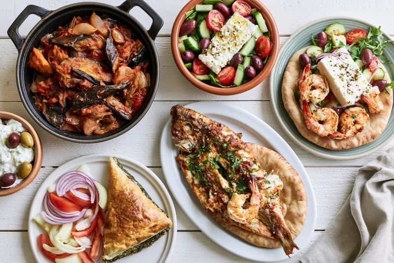 Greek mezze spread with grilled fish, shrimp, feta salads, and dips on white wooden table